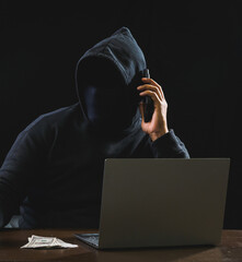 Wall Mural - Hacker spy man oneperson black hoodie sitting on table hand holding mobile phone looking computer laptop used login password attack security data digital internet network system, night dark background