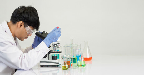 Wall Mural - Portrait asian man student scientist Wearing a doctor gown in the lab looking hand at chemist. caused by mixing reagents in scientific research laboratories with test tubes and microscope on the table