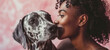 Close-up portrait of overjoyed African American young woman hugging her Dalmatian dog. Happy beautiful dark skinned girl with devoted pet. Isolated on pink background.