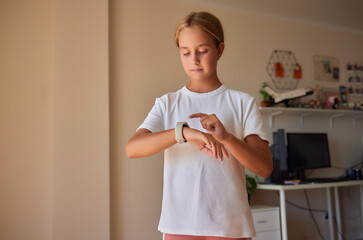 preteen girl puts modern smart watch on hands standing at home. Schoolgirl using touchscreen display on watches browsing internet