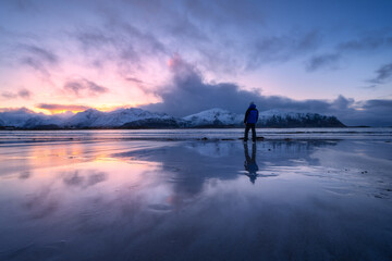 Wall Mural - man on the beach, snowy mountains and colorful sky at sunset
