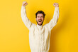 Cheerful young man in a white sweater is celebrating on a yellow background