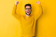 Portrait of a happy young man celebrating success isolated over yellow background