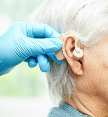 Wall Mural - Doctor install hearing aid on senior patient ear to reduce hearing loss problem.