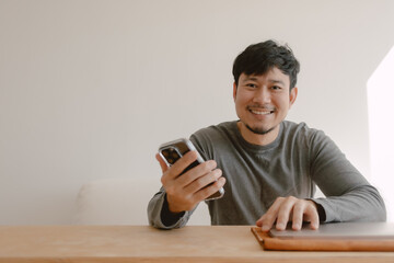 Wall Mural - Happy Asian man working on computer feeling happy with the app in mobile phone.