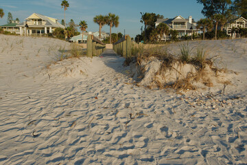 Horizontal view from Pass-a-grille Beach Florida towards shore. Footprints, wood beach access bridge, sea oats, green palm trees and blue sky in the background near sunset.