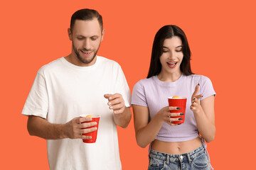 Wall Mural - Beautiful young couple with plastic cups of cold beer on orange background