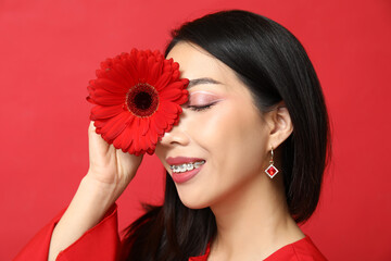 Sticker - Happy young Asian woman with beautiful gerbera flower on red background