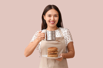 Poster - Young Asian woman adding sugar powder onto tasty pancakes on pink background