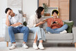 © Pixel-Shot - Teenage boy playing video game and his upset parents at home. Family problem concept