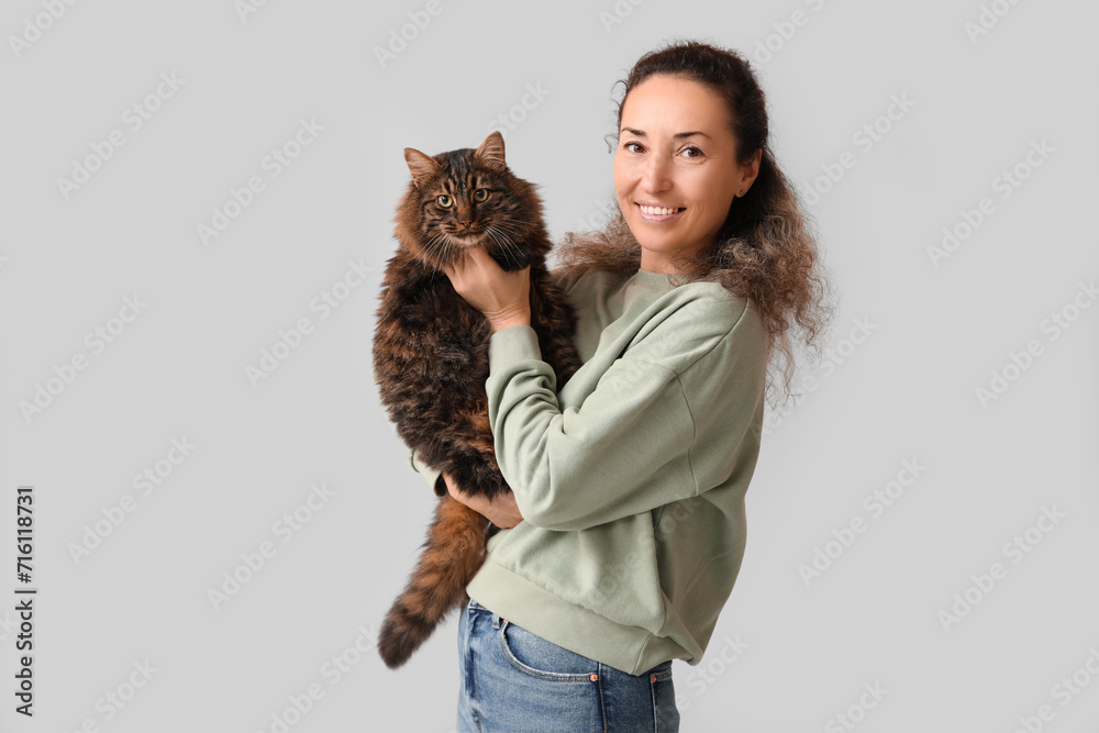 Beautiful mature woman with cute cat on grey background