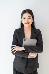 Wall Mural - Portrait of young asian woman in suit  smiling and holding digital tablet, standing over white background