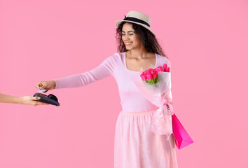 Sticker - Fashionable African-American woman with bouquet of flowers and shopping bags paying for purchases on pink background. International Women's Day celebration