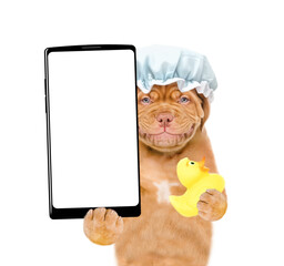 Poster - Smiling Mastiff puppy wearing shower cap holds rubber duck and shows big smartphone with white blank screen in it paw. isolated on white background