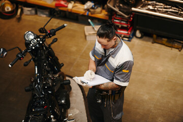 Wall Mural - Mechanic examining broken motorcycle of client and taking notes in document