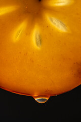 Wall Mural - Slice of orange persimmon with juice drops on a black background, macro photography. Texture fresh fruit, closeup