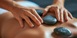 © Valeriia - Close-up woman's back enjoying exotic hot stones spa massage. Relaxed woman lying on a spa bed while the masseuse is putting hot stones on her back. Spa treatment concept