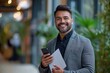 © sirisakboakaew - An attractive Latino businessman holding documents in his hands with a happy smile and a bearded head