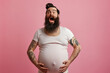 © Valeriia - Excited pregnant adult trans man with beard expectant father on pink background. Diversity in parenthood pregnant man challenging gender norms and expanding the definition of family concept