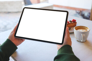 Mockup image of a woman holding digital tablet with blank white desktop screen in cafe