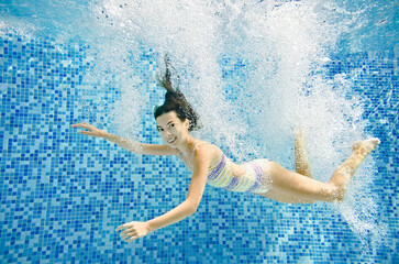 Wall Mural - Child swims underwater in swimming pool, active little girl jumps, dives and has fun under water, kid fitness and sport on family vacation 
