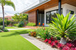 © Kien - A contemporary Australian home or residential buildings front yard features artificial grass lawn turf with timber edging, and a big flowers garden