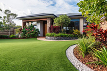 A Contemporary Australian Home Or Residential Buildings Front Yard Features Artificial Grass Lawn Turf With Timber Edging, And A Big Flowers Garden