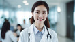 © Pasindu - A beautiful Asian female doctor is smiling at the camera while standing in the background of a hospital.