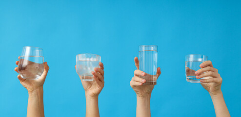 Water in transparent glasses in the hands of women, on a blue background.