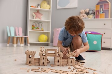 Poster - Little boy playing with wooden construction set on floor in room, space for text. Child's toy