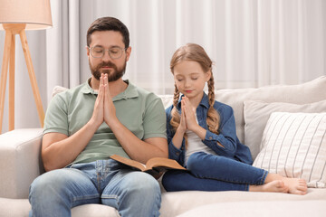 Wall Mural - Girl and her godparent praying over Bible together on sofa at home