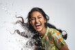Studio portrait of a joyful young woman of Indian ethnicity having long flowing hair playing with water