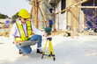 © ฺฺฺBoonterm - Female engineer foreman sitting holds laptop computer setup and checks  modern technology tools laser level and vertical marker (Plum Bob) on tripod at construction site, condominium building.