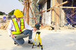 © ฺฺฺBoonterm - Female engineer foreman sitting holds laptop computer setup and checks  modern technology tools laser level and vertical marker (Plum Bob) on tripod at construction site, condominium building.