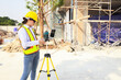 © ฺฺฺBoonterm - Female engineer foreman holds laptop computer setup and checks  modern technology tools laser level and vertical marker (Plum Bob) on tripod at construction site, condominium building.