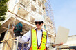 © ฺฺฺBoonterm - Female engineer foreman holds laptop computer setup and checks  modern technology tools laser level and vertical marker (Plum Bob) on tripod at construction site, condominium building.