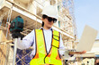 © ฺฺฺBoonterm - Female engineer foreman holds laptop computer setup and checks  modern technology tools laser level and vertical marker (Plum Bob) on tripod at construction site, condominium building.