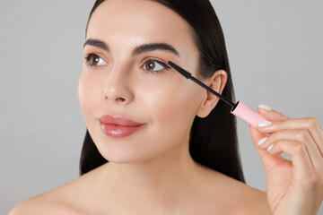 Poster - Beautiful young woman applying mascara on grey background, closeup