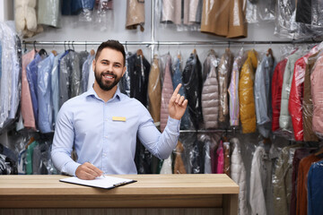 Wall Mural - Dry-cleaning service. Happy worker pointing at something at counter indoors, space for text