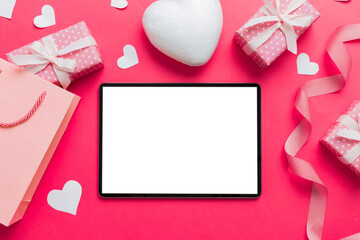 Wall Mural - Top view of digital tablet with gift boxes and hearts on colorful background. Tablet with black screen with Holiday decorations gift box top view