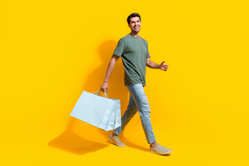 Poster - Full length photo of excited cheerful man dressed khaki t-shirt holding bargains walking isolated yellow color background