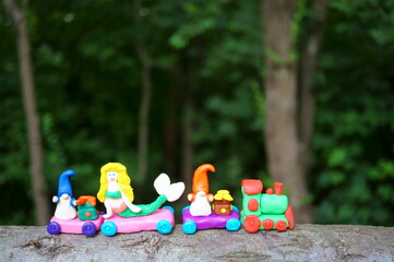 A toy train made of plasticine with a mermaid, gnomes and gifts. Children's toy decorations for the holiday and New year.