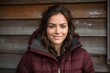 © CogniLens - Portrait of a grinning woman in her 20s sporting a quilted insulated jacket against a rustic wooden wall. AI Generation