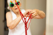 © Austockphoto - elderly lady in fun Christmas glasses trying to untangle string of red beads