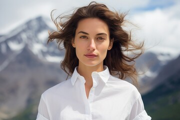 Wall Mural - Portrait of a merry woman in her 20s wearing a classic white shirt against a snowy mountain range. AI Generation
