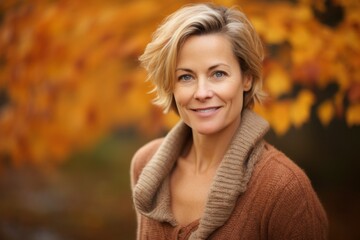 Wall Mural - Portrait of a happy woman in her 50s dressed in a warm wool sweater against a background of autumn leaves. AI Generation
