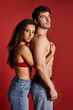 © LIGHTFIELD STUDIOS - brunette and charming young woman in lace bra and jeans embracing her muscular man on red background