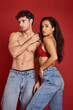 © LIGHTFIELD STUDIOS - muscular and shirtless man in jeans standing with gorgeous brunette woman in bra on red backdrop
