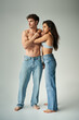 © LIGHTFIELD STUDIOS - brunette young woman in satin bra and jeans embracing shirtless man on grey background, affection
