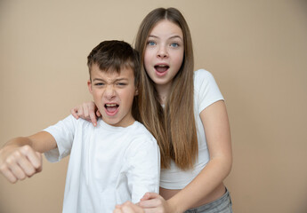 Wall Mural - beautiful pretty 14 years old girl with her cute and cool 11 years old brother in front of brown background, brother and sister love